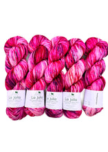 Five skeins of pink and red yarn with 'La Jolla' labels on a white background pink and white variegated with navy speckles